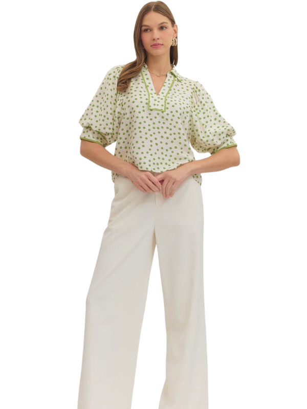 Woman wearing a green patterned top and white pants on a white background
