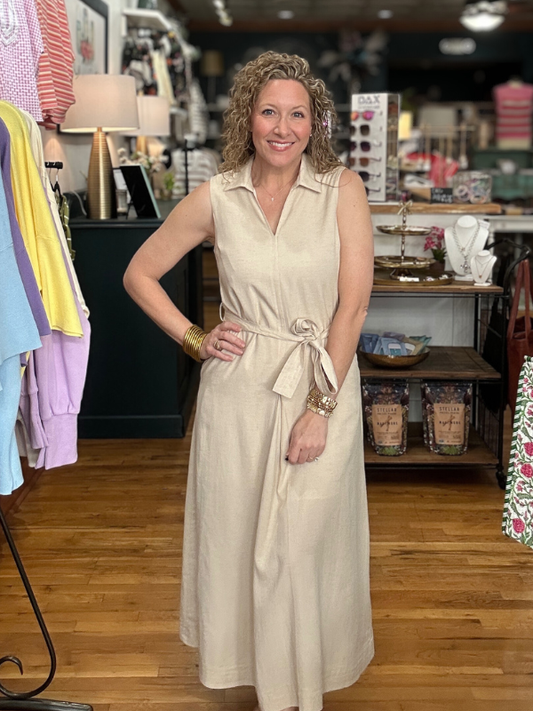Woman in a beige dress standing in a store with various items on shelves and racks.