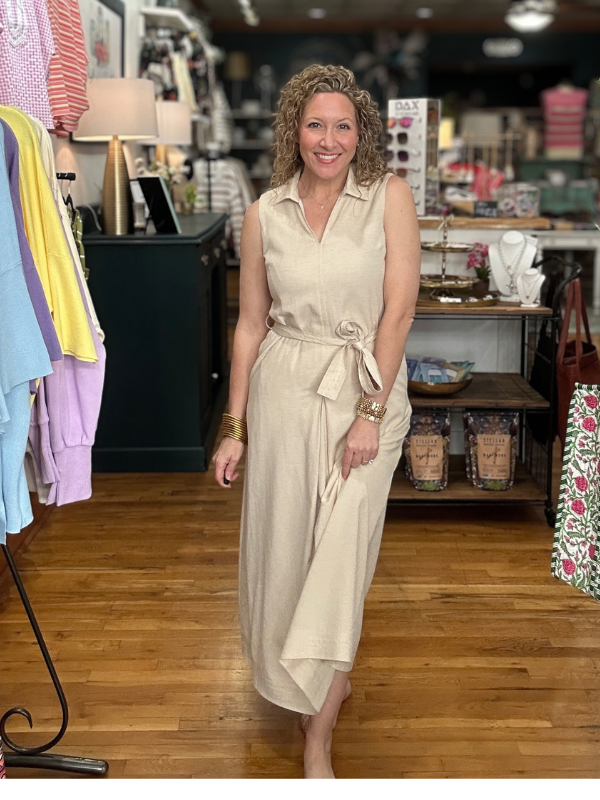Woman in a beige dress standing in a store with clothing and products in the background