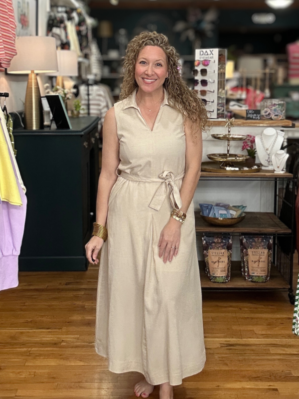 Woman in a beige dress standing in a store with shelves and products in the background