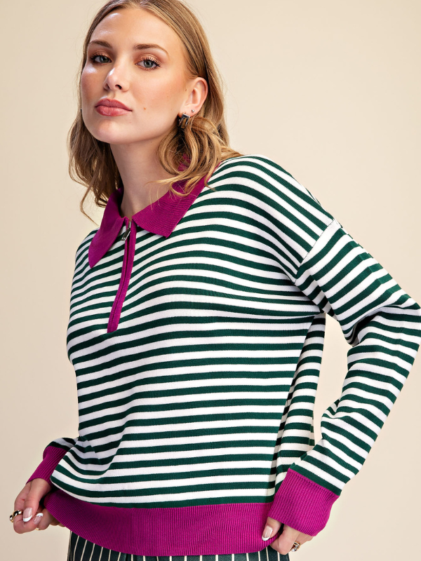 A woman wearing a long-sleeve knit polo-style sweater with horizontal dark green and white stripes, featuring a magenta collar, placket, cuffs, and hem, posed against a solid beige background.