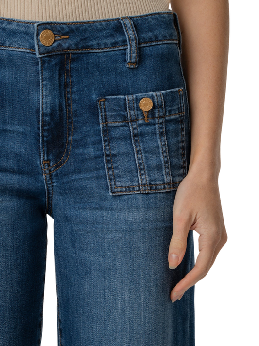 Close-up of a person wearing blue denim jeans, showing the front waistband, belt loops, front pocket, and hand resting against the thigh, on a white background.