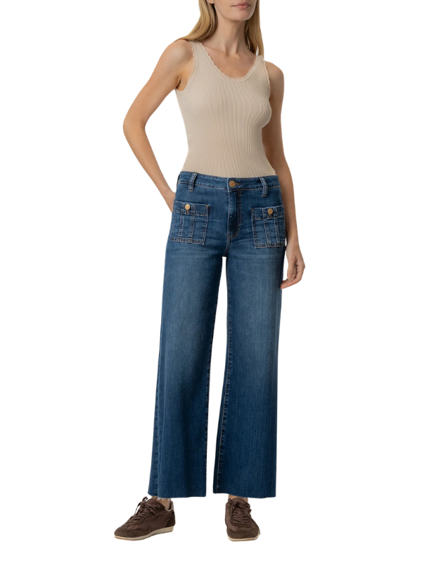 A model wearing a pair of wide-leg blue denim jeans with front patch pockets, paired with a beige ribbed tank top and brown sneakers, shown against a plain white background.