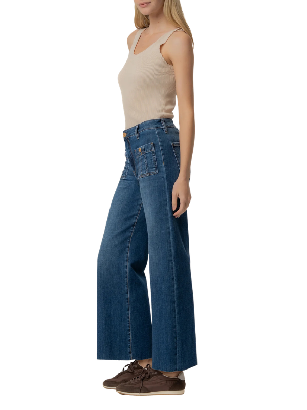 A woman modeling a pair of high-waisted, wide-leg blue jeans with a beige tank top and brown shoes, shown from a side profile against a plain white background.
