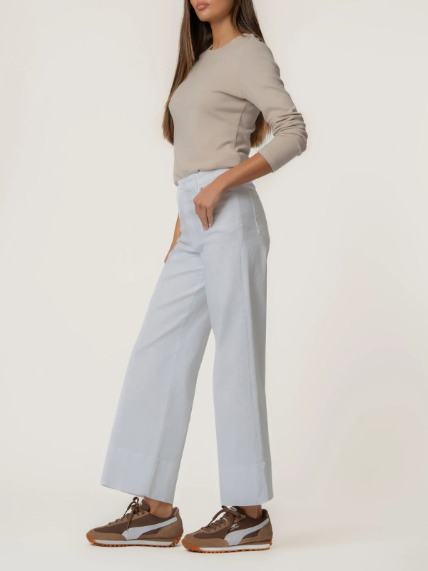 Person wearing a beige sweater and light white pants on a white background