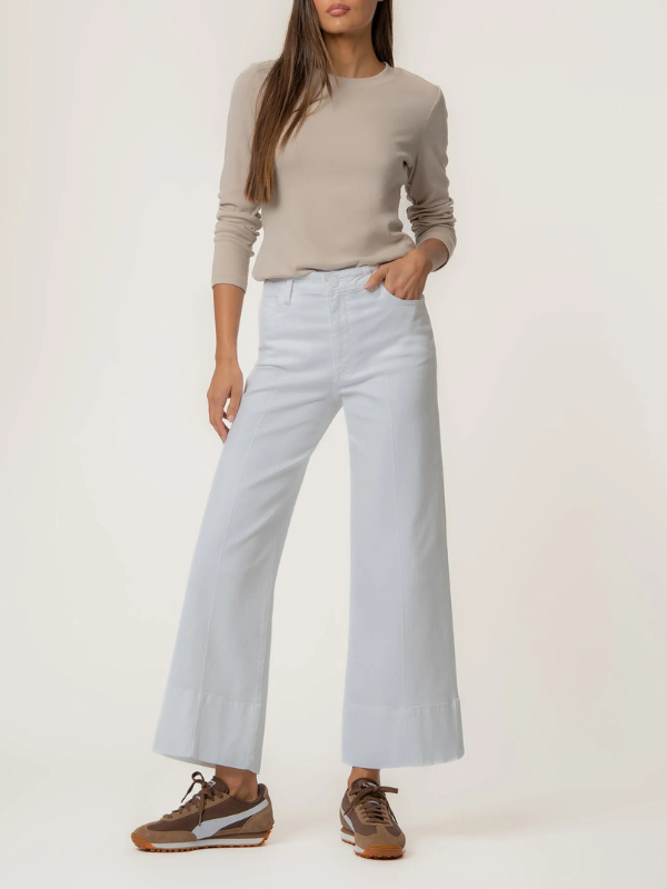 Person wearing a beige long-sleeve top and light blue wide-leg pants on a white background