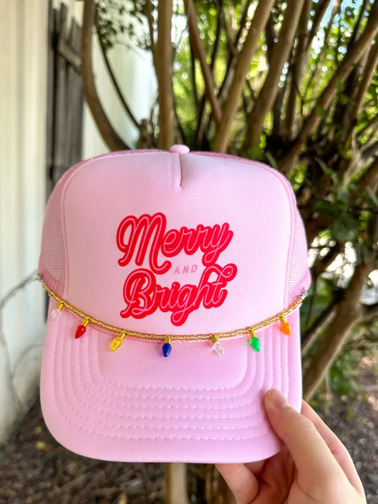 Pink cap with 'Merry and Bright' text and colorful tassels, held outdoors.