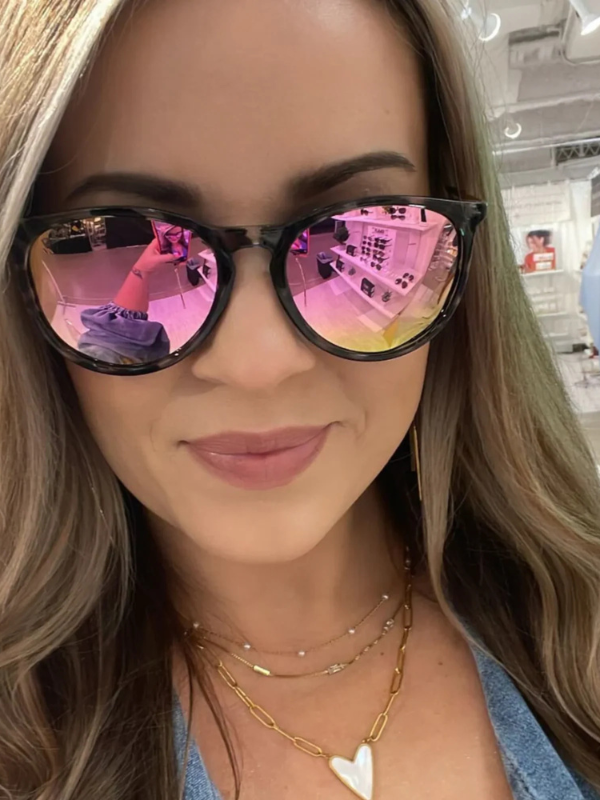 Person wearing black sunglasses with pink reflection, indoors.