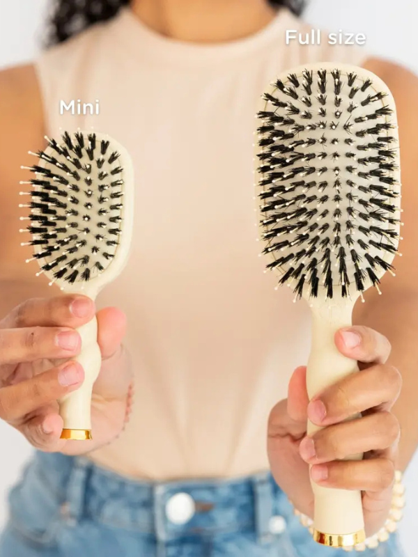 Mini and full size hairbrushes held by a person against a neutral background