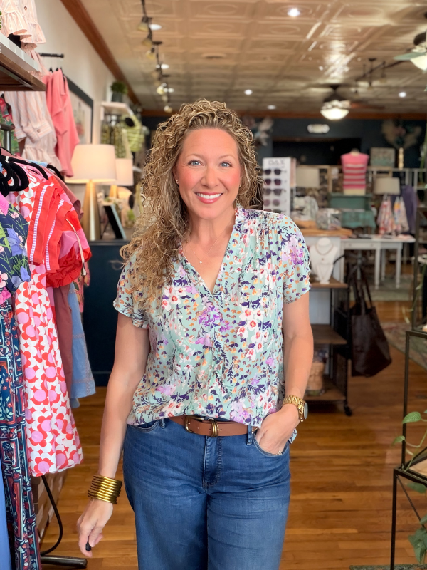 Woman in a floral shirt and jeans standing in a clothing store.