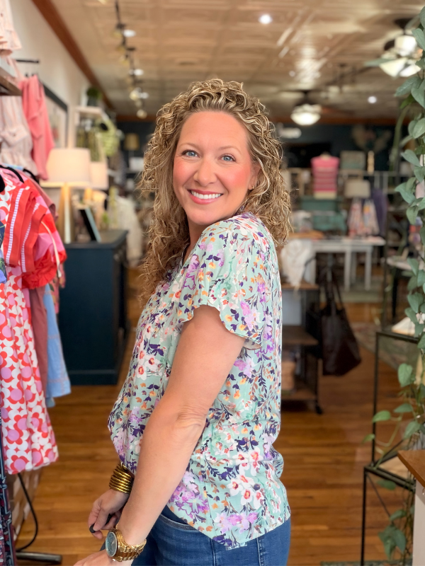 Woman in a floral shirt standing in a store with clothing and decor in the background