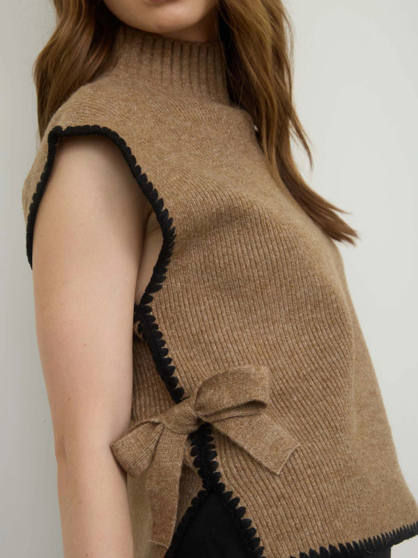 Brown knitted vest with black trim and a bow detail on a plain background