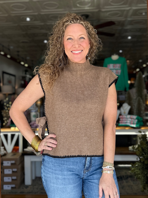 Woman wearing a brown sleeveless sweater with a store interior in the background
