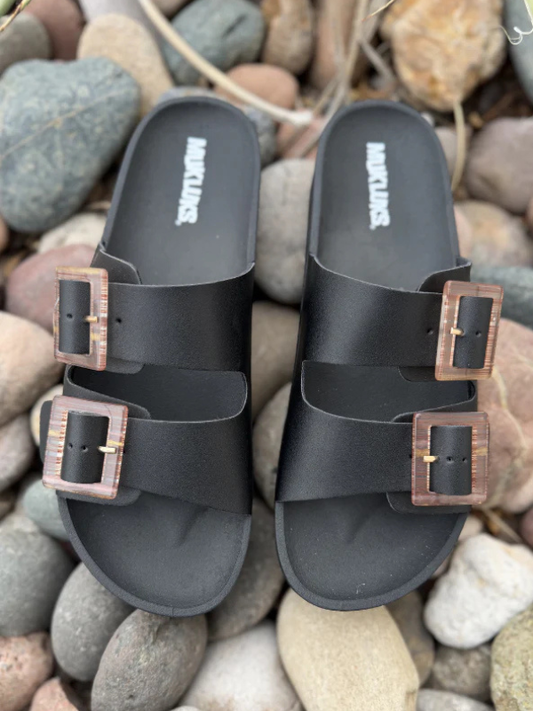 Black sandals with brown buckles on a pebble surface