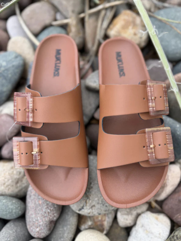 Pair of brown sandals with clear straps on a pebble background