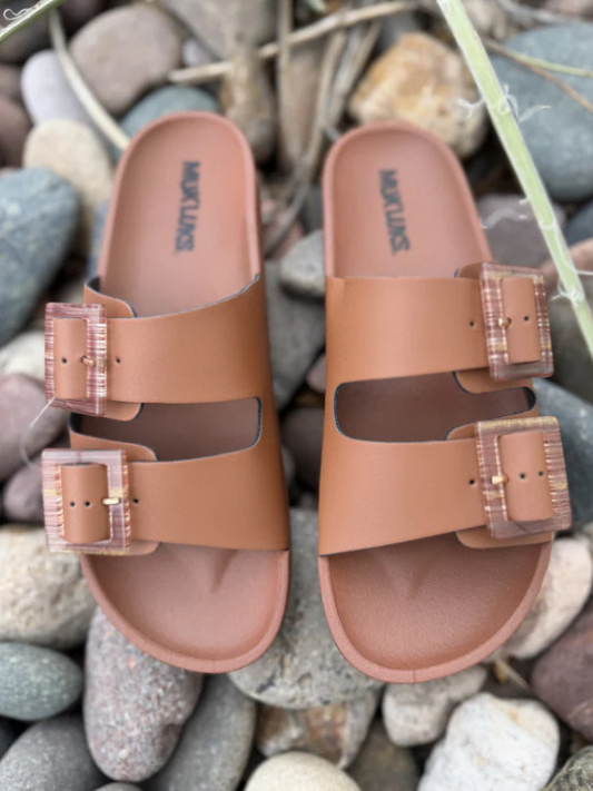 Pair of brown sandals with clear straps on a pebble background