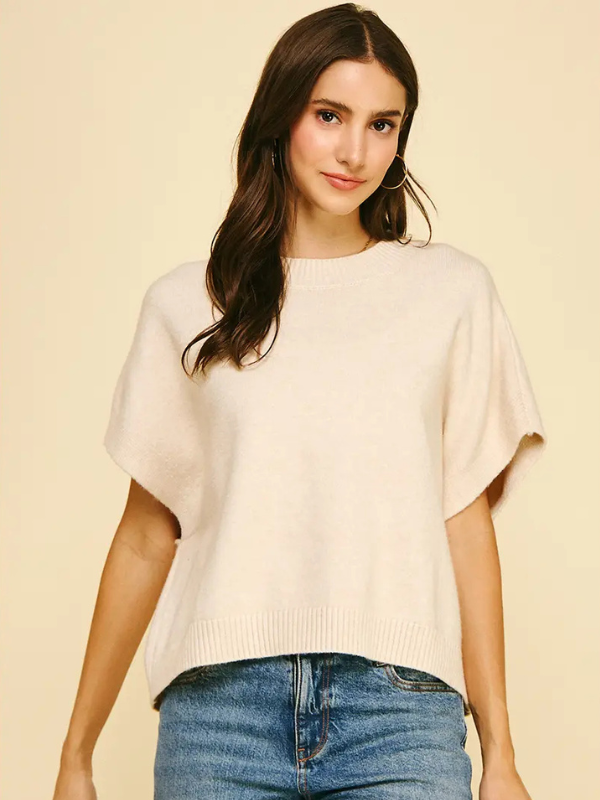 Woman wearing a beige sweater and blue jeans against a beige background