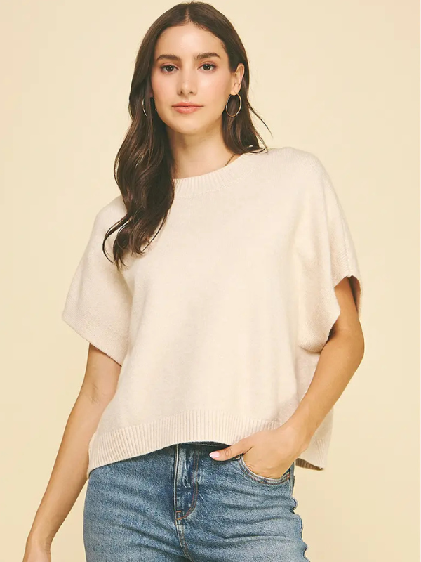 Woman wearing a beige sweater and blue jeans on a plain background