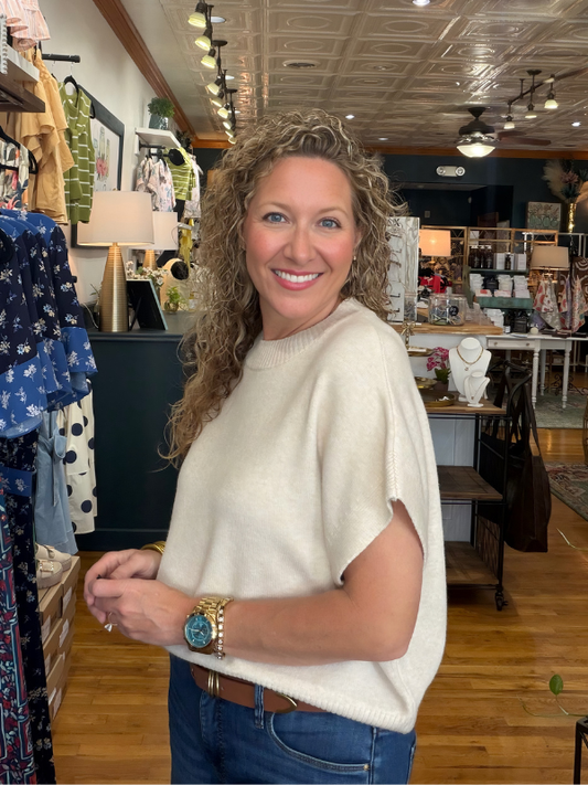 Woman in a store wearing a white sweater and blue jeans, smiling.
