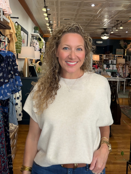 Woman in a white sweater standing in a store with clothing racks in the background