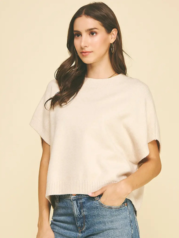 Woman wearing a beige sweater and blue jeans against a beige background