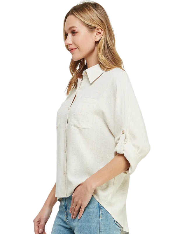 A woman wearing a light beige linen button-up shirt with rolled-up sleeves and blue jeans, shown from a side profile against a white background.