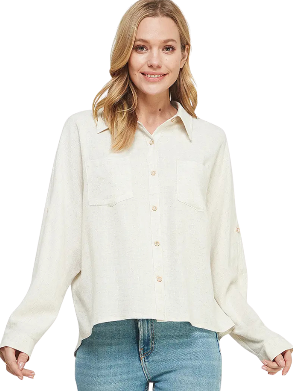 A woman wearing a light cream-colored, long-sleeve linen button-up shirt with two chest pockets and blue jeans, photographed against a solid white background.