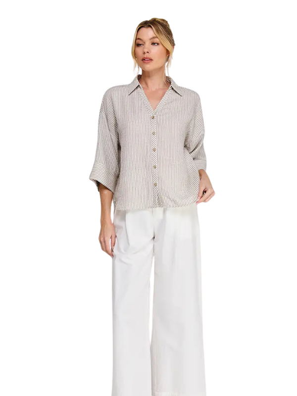 A woman modeling a light beige and white vertically striped button-down shirt with three-quarter sleeves, paired with white wide-leg pants, against a plain white background.