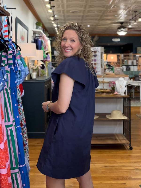 Woman in a navy dress standing in a store with clothing racks and displays.