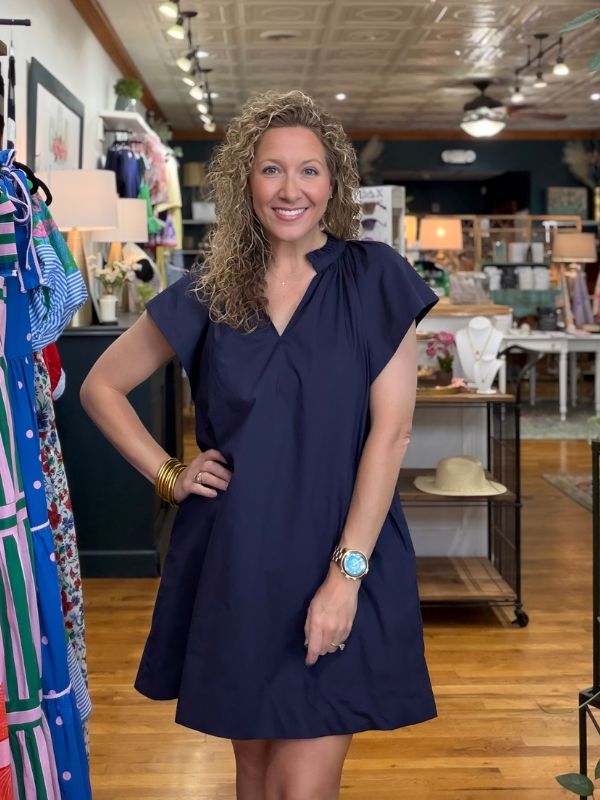 Woman in a navy dress standing in a store with clothing racks and products in the background.
