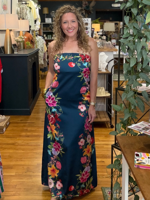 Woman wearing a floral dress standing in a store with plants and furniture.