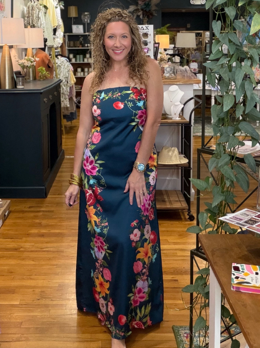 Woman in a floral dress standing in a store with wooden floors and shelves.