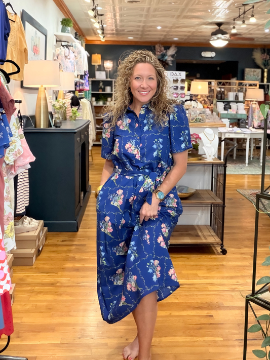 Woman in a blue floral dress standing in a store with wooden floors and shelves.