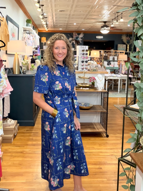 Woman in a blue floral dress standing in a store with wooden floors and shelves.