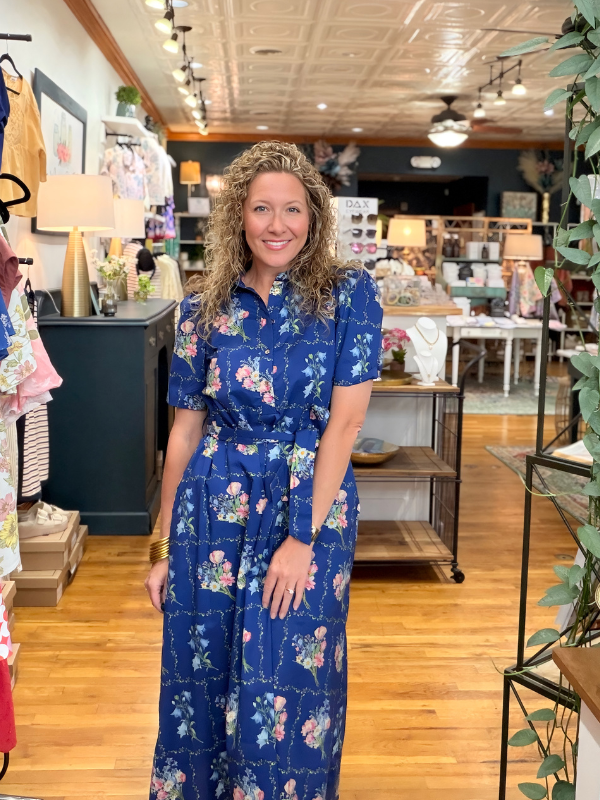 Woman in a blue floral dress standing in a store with wooden floors and shelves.