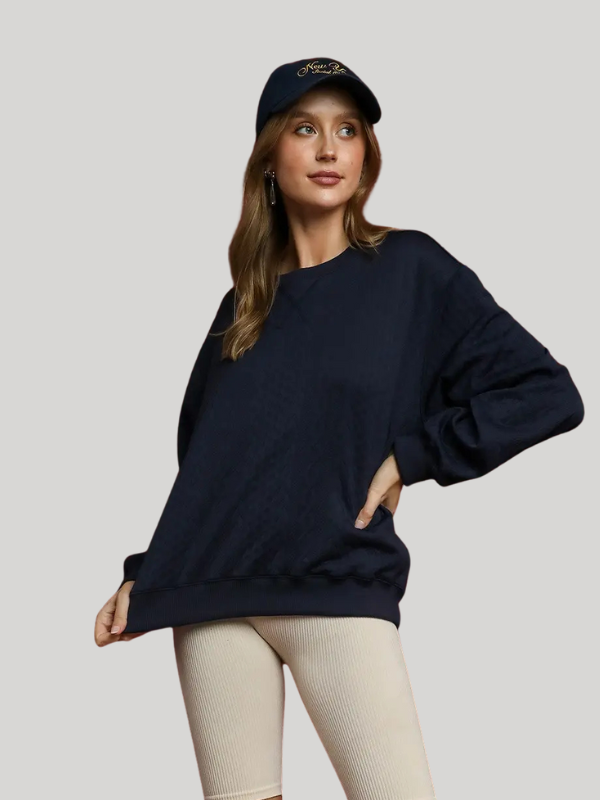 Woman wearing a navy blue oversized sweater and cap on a light gray background