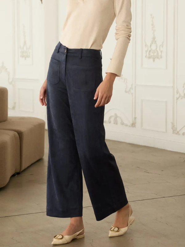 A person wearing dark navy wide-leg cropped trousers, a cream long-sleeve top, and cream pointed flats, standing in a bright interior with paneled walls and a beige sofa.