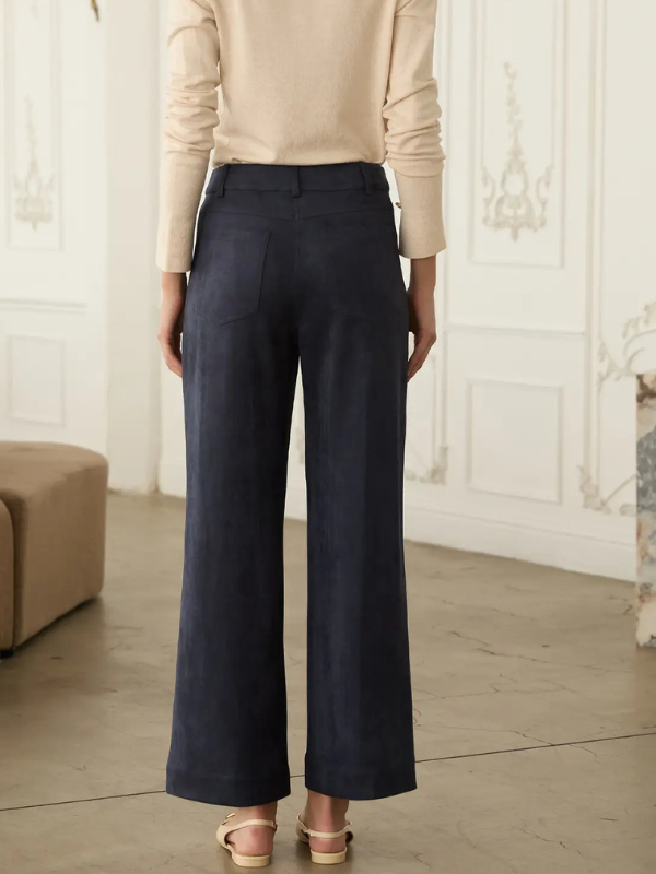 A person shown from the back wearing dark navy wide-leg cropped trousers, a beige long-sleeve top, and beige sandals in an indoor room with paneled walls.