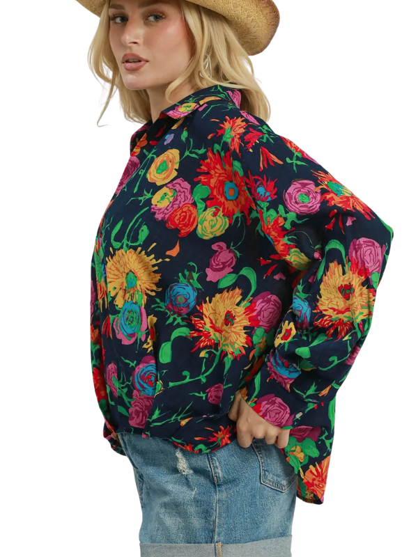 A woman wearing a dark navy floral button-up shirt with a vibrant multicolor print, paired with blue jeans and a straw hat, shown from a side profile against a white background.