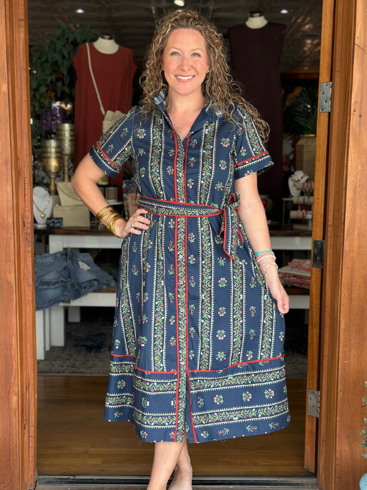 Woman wearing a blue patterned dress standing in a store doorway.