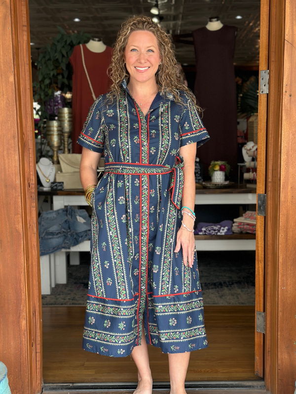 Woman wearing a blue patterned dress standing in a store doorway.