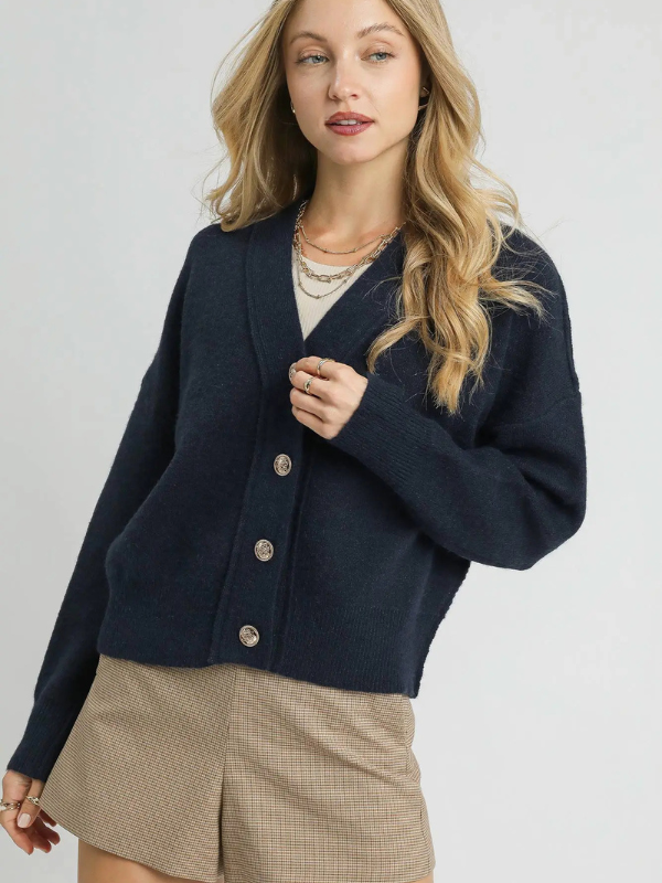 Woman wearing a navy cardigan over a beige outfit on a plain background