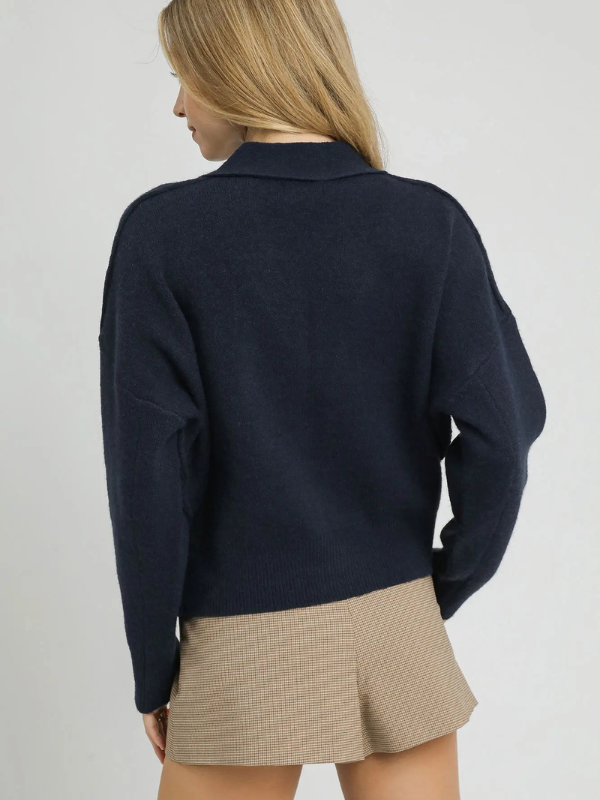 Person wearing a navy sweater and beige skirt on a plain background