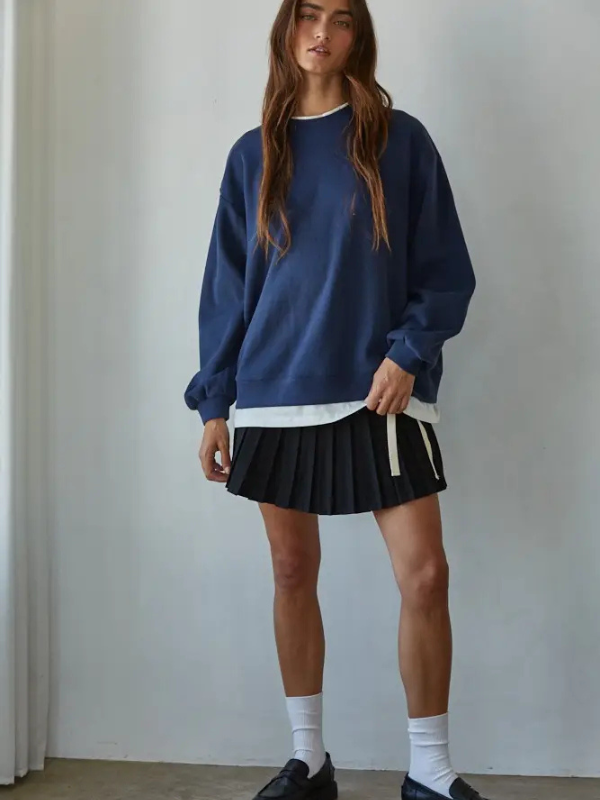 Person wearing a blue sweatshirt and black skirt against a plain background