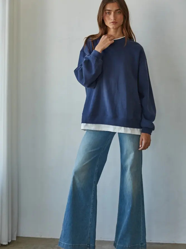 Woman wearing a navy sweater and blue jeans against a plain background