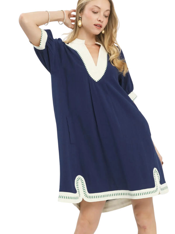 A woman modeling a loose navy blue tunic dress with contrasting cream trim on the V-neck, sleeve cuffs, and hem, set against a plain white background.