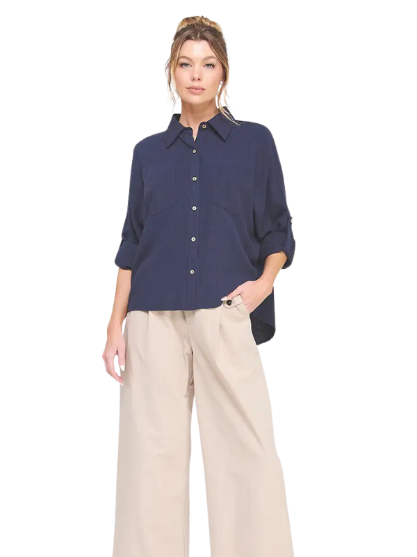 A woman modeling a navy blue button-up shirt with three-quarter sleeves and beige wide-leg pants against a plain white background.
