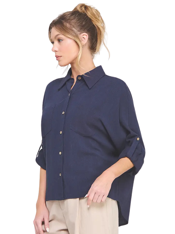 A woman wearing a navy blue button-down shirt with rolled-up sleeves and beige pants, shown from a side profile against a plain white background.