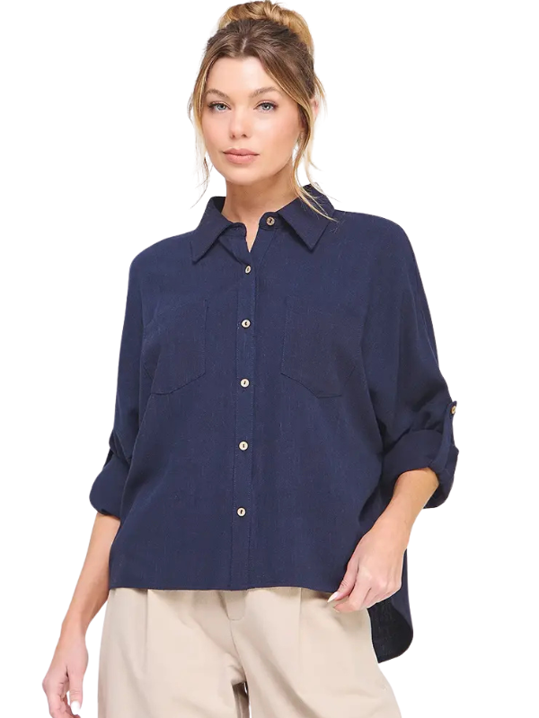 A woman wearing a navy blue button-down shirt with three-quarter sleeves and beige pants, photographed against a plain white background.