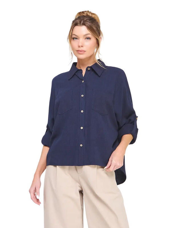 A woman modeling a navy blue button-down shirt with beige pants against a plain white background.